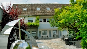 A courtyard with a modern sculpture, a building with a tiled roof, and outdoor seating. - Hotel Herrenhof (Lübeck)