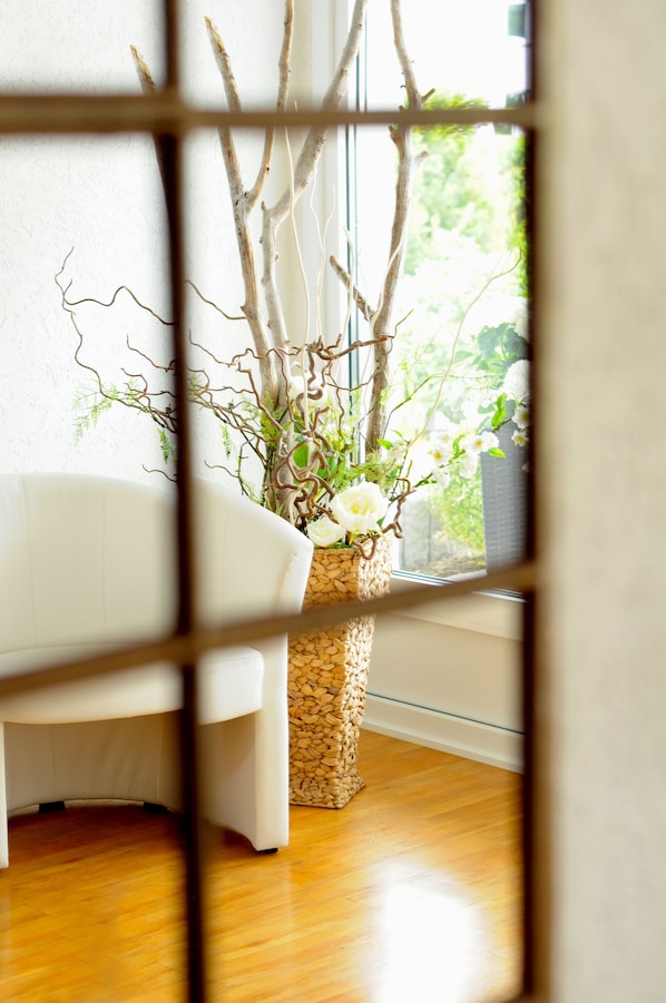 A room with a white sofa, a woven basket with branches and flowers, and a view through a window.