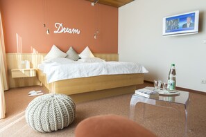 A bedroom with a bed, a bedside table, a clear glass coffee table, a knitted pouf, and a wall with the word "Dream" written on it. - Hotel Strandhus (Cuxhaven)