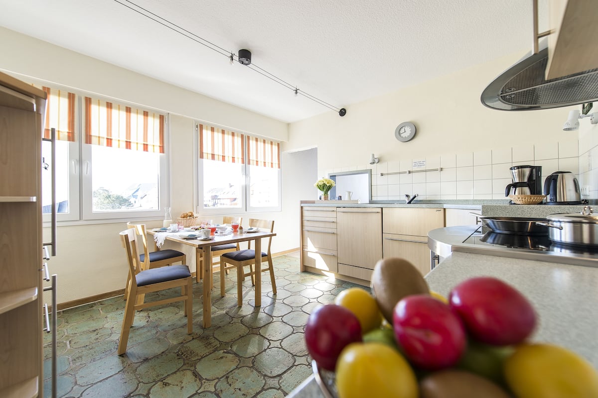 A kitchen with a dining table, chairs, a fruit bowl, and a stove.