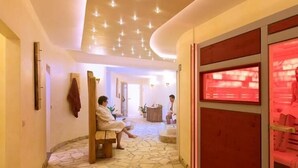 Ein Wellnessbereich mit Steinboden, Holzbanken und einem rot beleuchteten Behandlungsraum.