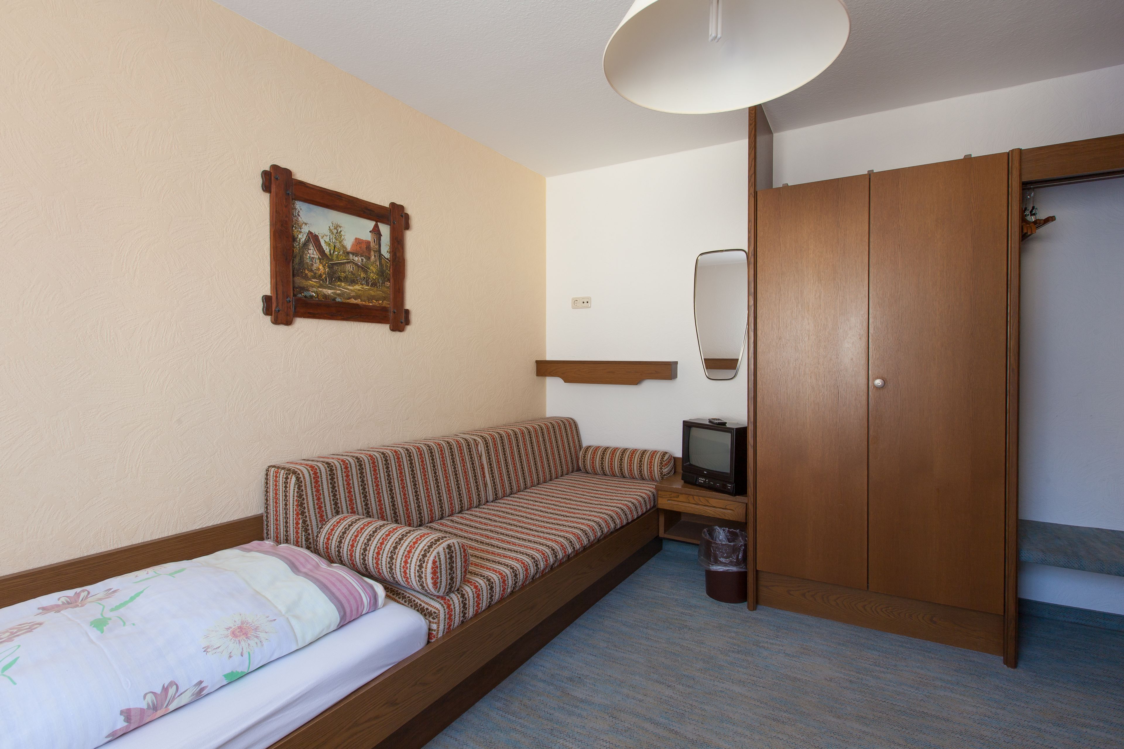 A small room with a sofa, a television, a wooden wardrobe, and a painting on the wall.