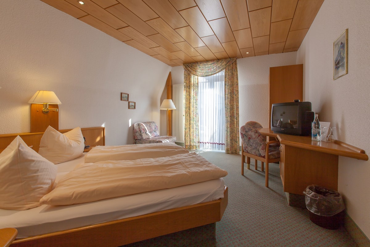 A hotel room with two beds, a desk with a television, a chair, and a small trash bin.