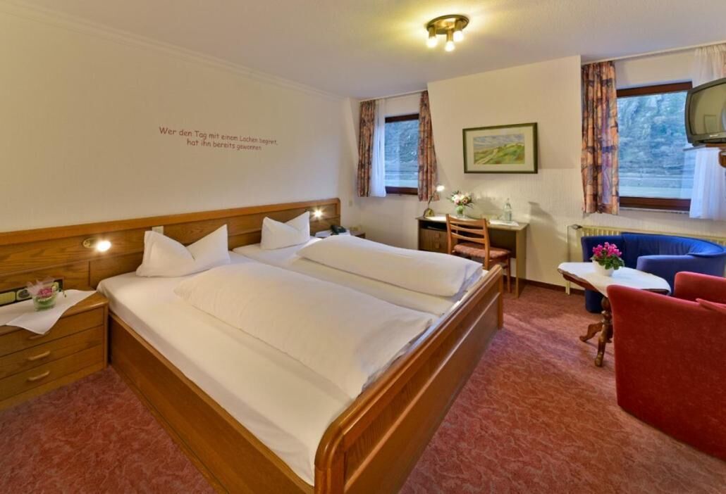 A hotel room with a double bed, a desk, a chair, a TV, and a window with curtains.