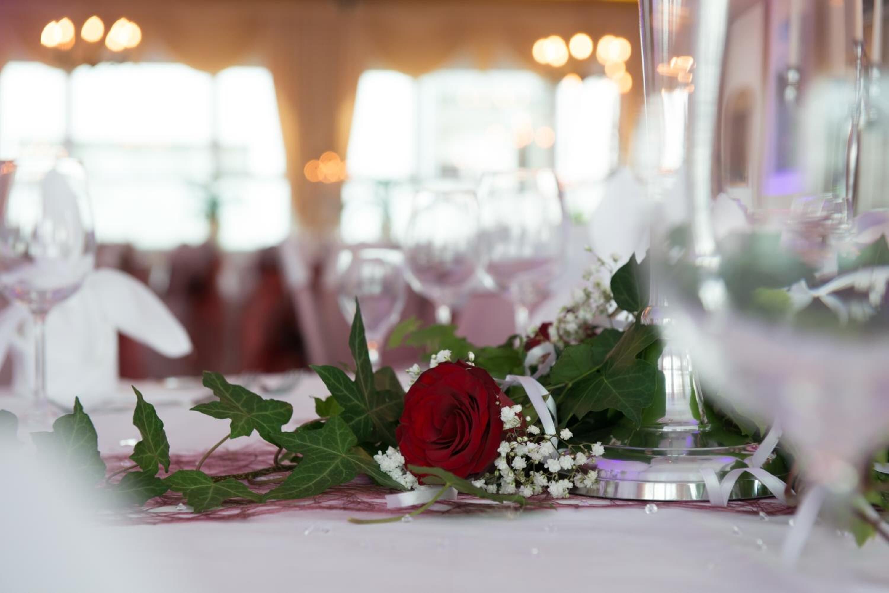 A table setting with a red rose, white flowers, and green leaves.