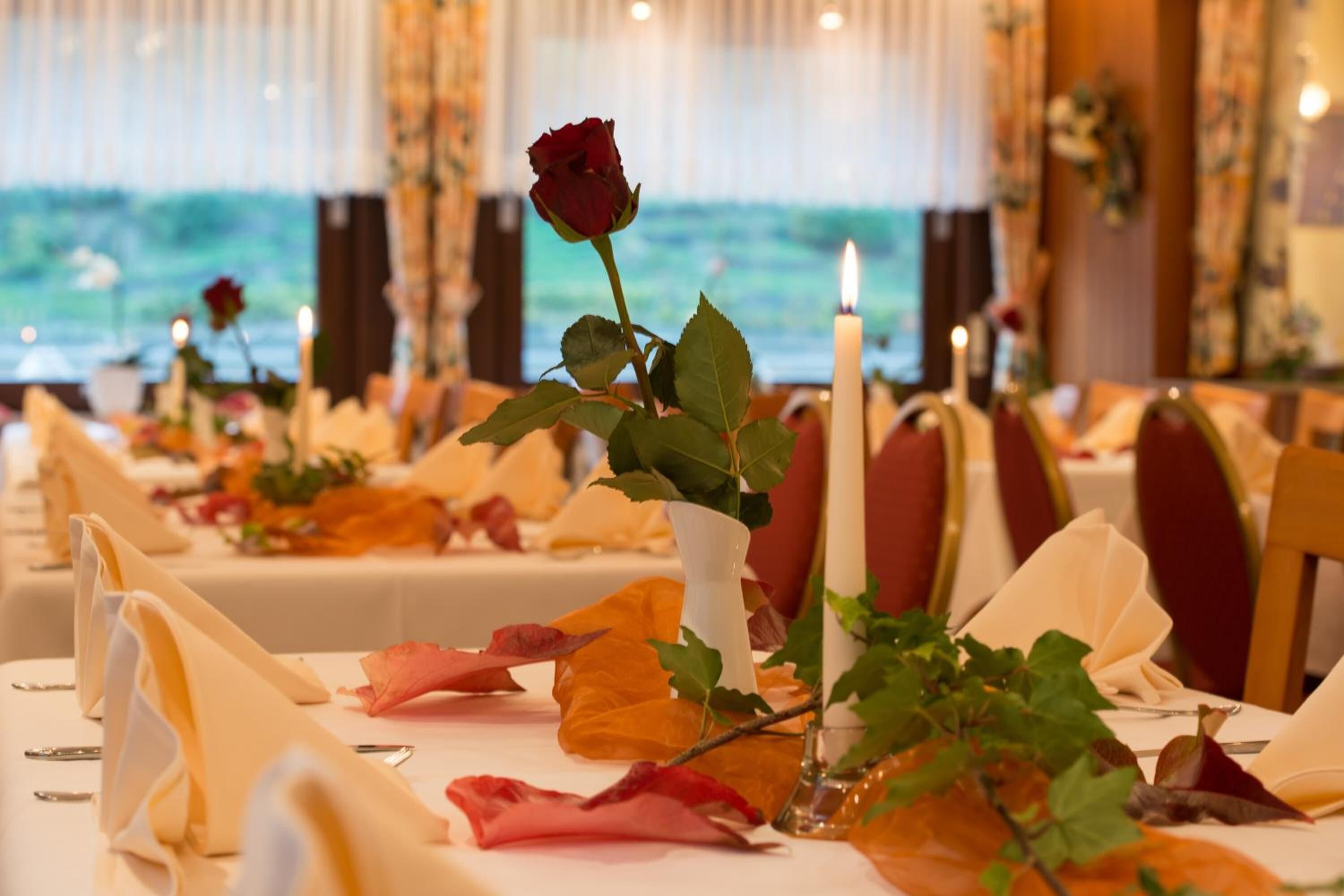 Una mesa de comedor adornada con un jarrón con una sola rosa, velas y hojas otoñales.