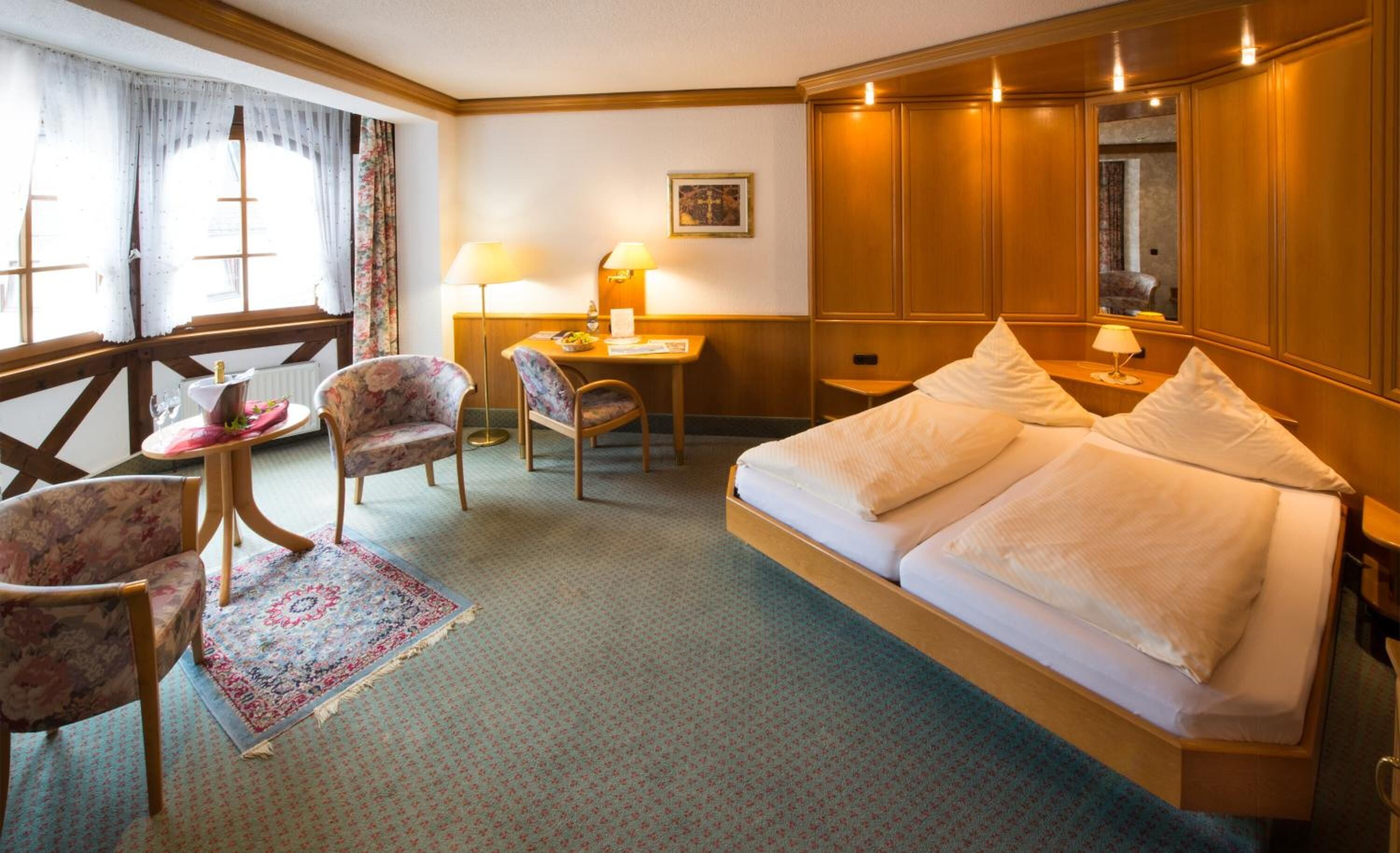 A hotel room with a bed, two chairs, a desk, a lamp, and a window with curtains.