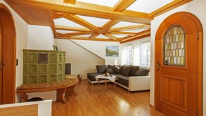 Ein geräumiges Wohnzimmer mit Holzbalkendecke, einem grünen Schrank, einer Couch und einer Tür mit bleiverglastem Fenster.