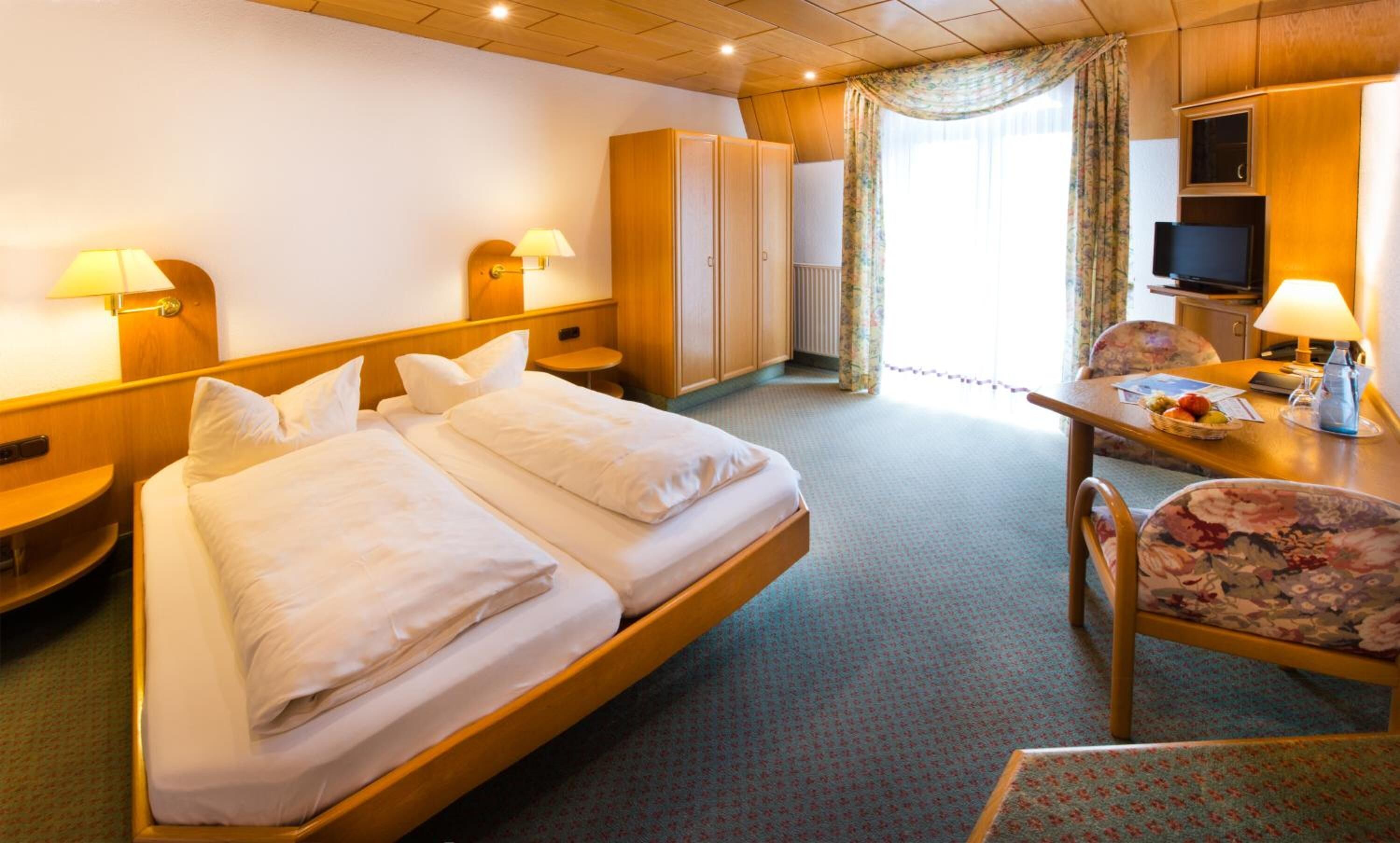 A hotel room with a double bed, a desk with a chair, a television, and a wardrobe.