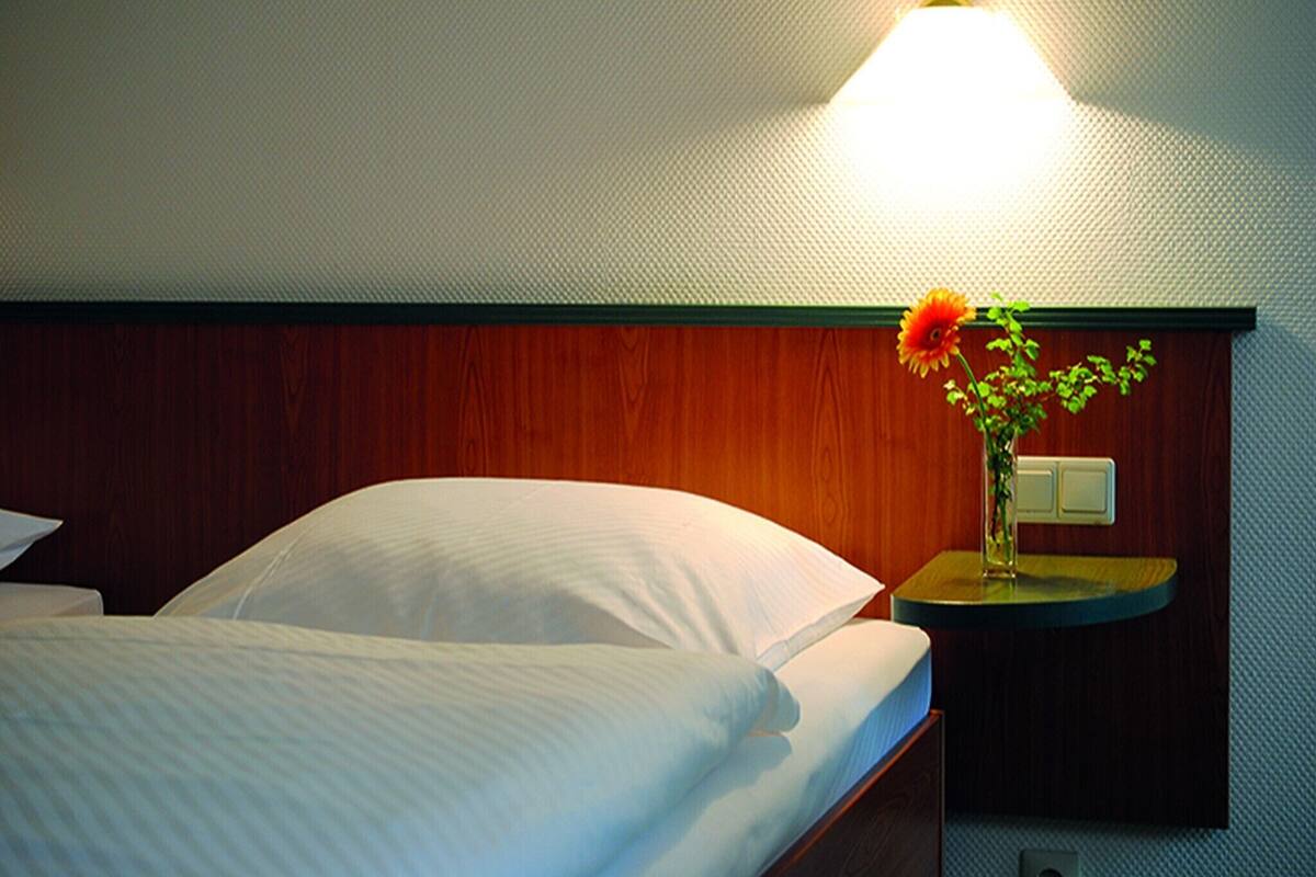 Ein Hotelzimmer mit einem Bett, einem Nachttisch mit Blumenvase und einer Wandleuchte.