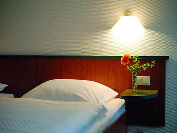 A hotel room with a bed, a nightstand with a vase of flowers, and a wall-mounted light.