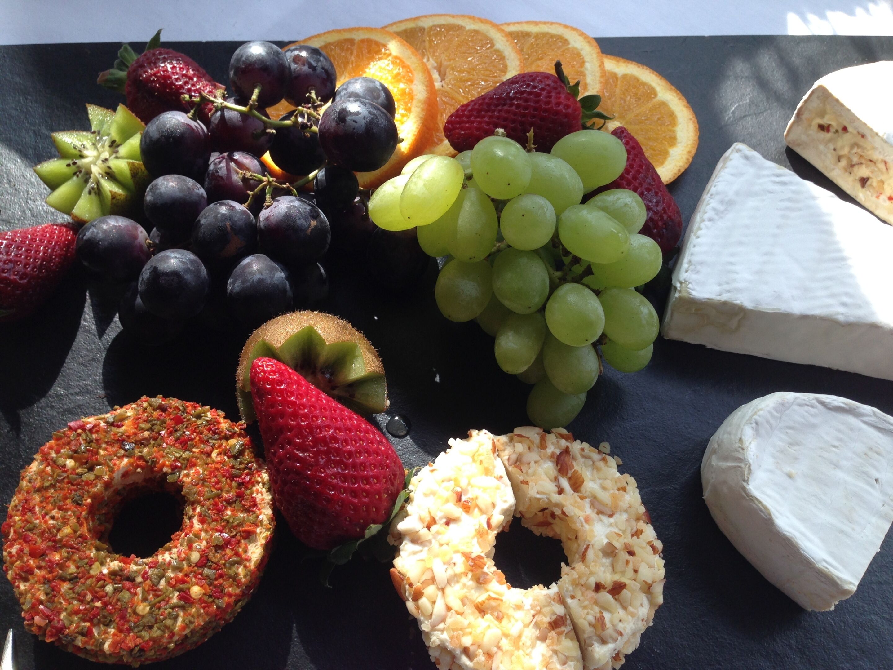 A selection of fruits and cheeses on a slate board.