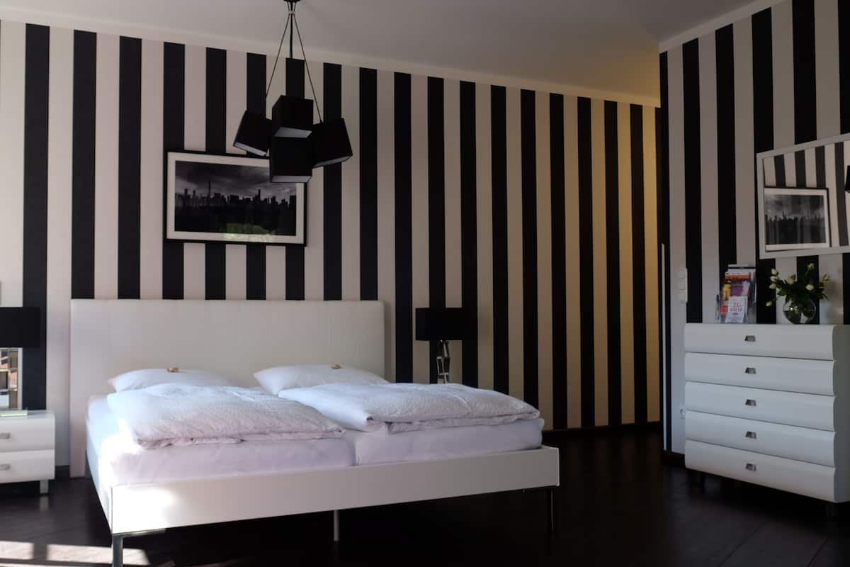 A modern bedroom with a large bed, a nightstand, a dresser, and a black and white striped wall.