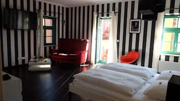 A room with black and white striped walls, a red armchair, a white bed, and a red chair.