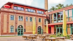 A building with a brick facade, multiple windows, and outdoor seating with yellow umbrellas. - Backstage Hotel (Dresden)