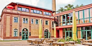 A building with a brick facade, multiple windows, and outdoor seating with yellow umbrellas.