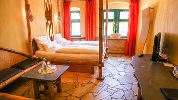 A room with a bed, a small table with bottles, a chair, and a TV.