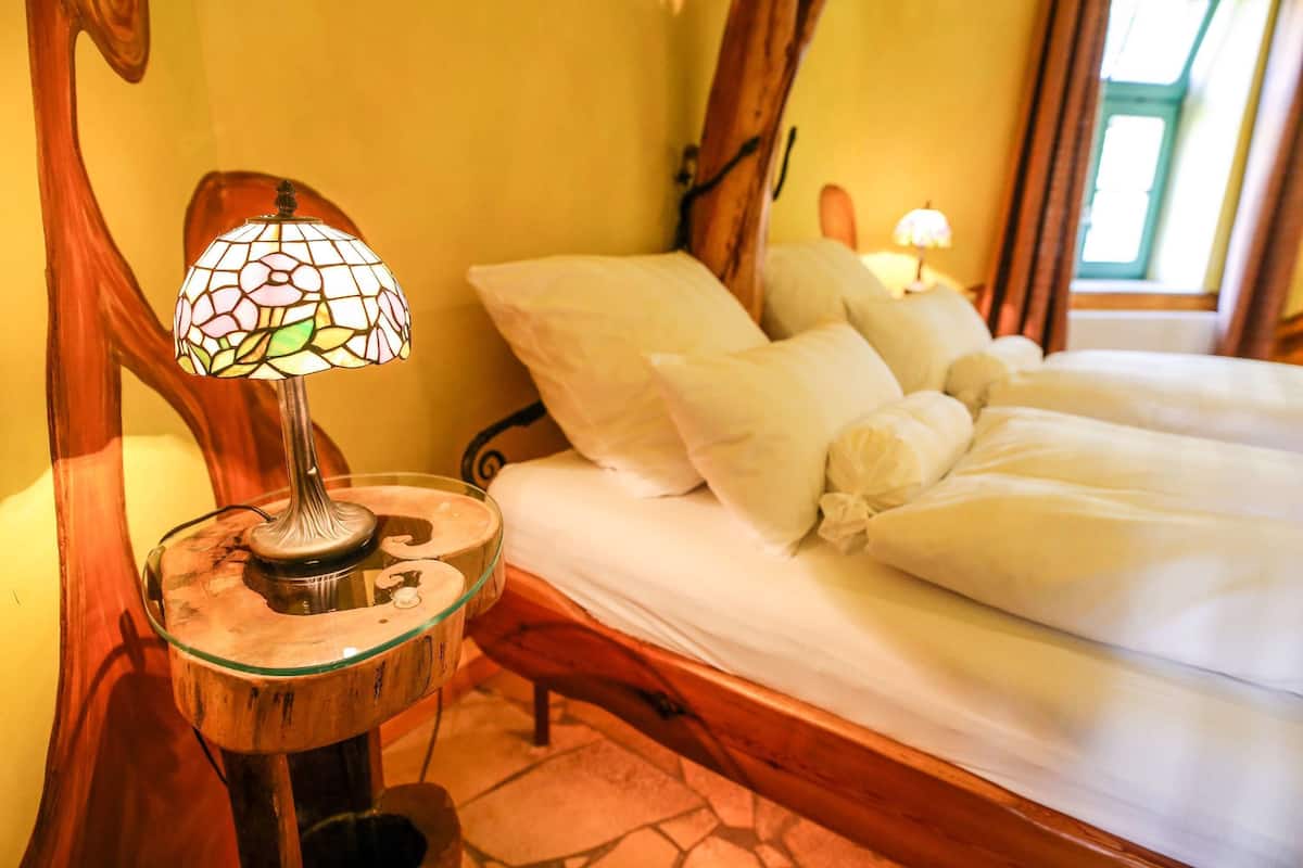 A bed with white linens and a glass table lamp with a stained glass shade.