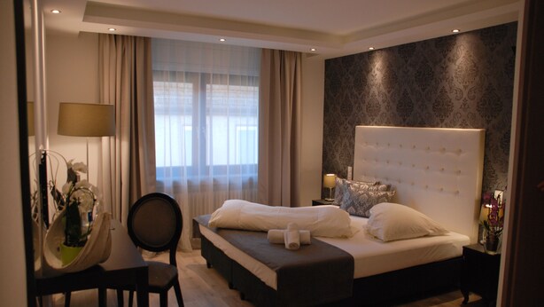 A modern hotel room with a large bed, a desk with a chair, and a window with curtains. - Hotel Zur Linde (Hanau)
