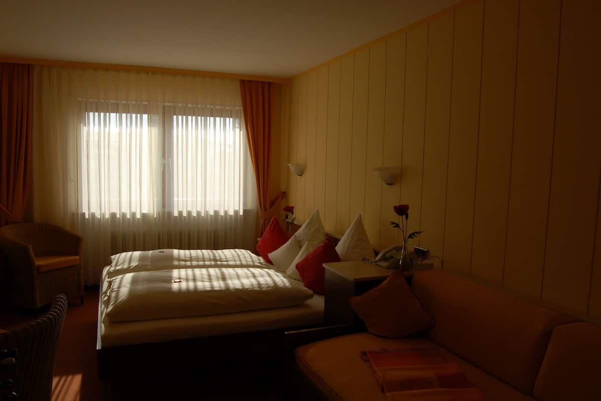 A hotel room with a bed, a sofa, a chair, and a desk with a telephone.