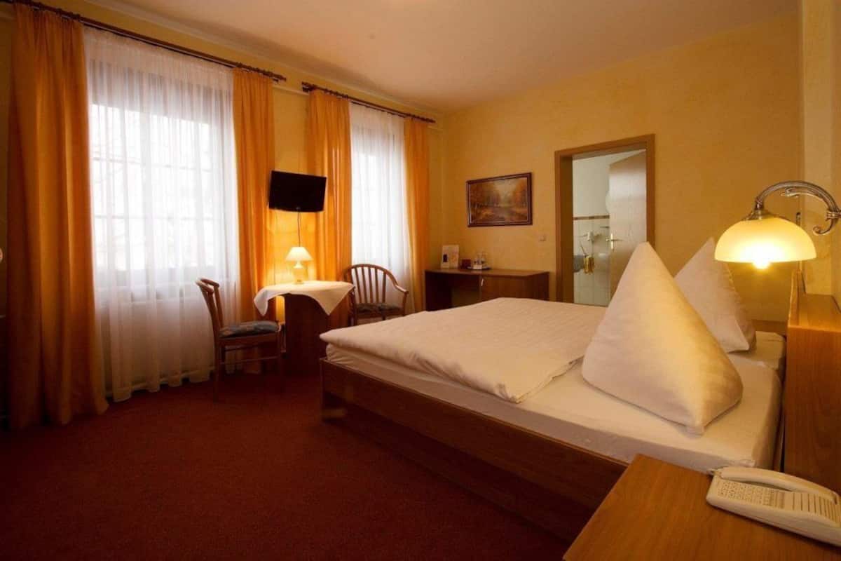 A hotel room with a bed, a desk, a chair, a lamp, a telephone, and a painting on the wall.