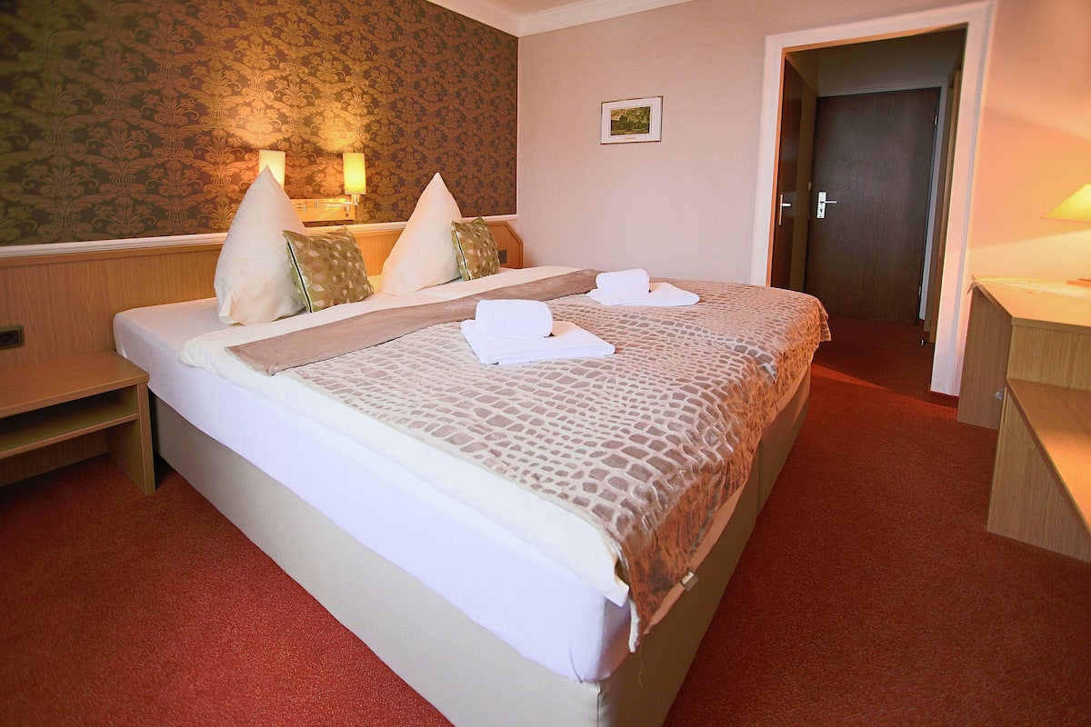 A hotel room with a bed, bedside tables, a desk, and a door.