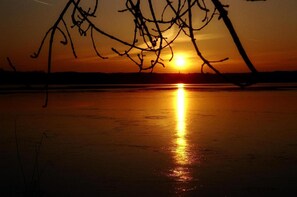 A sunset over a calm body of water with silhouettes of trees in the foreground. - Alter Krug Kallinchen (Zossen)