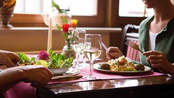 Una mesa de comedor con un posavasos rosa, una ensalada, un plato de pasta y dos copas de vino.