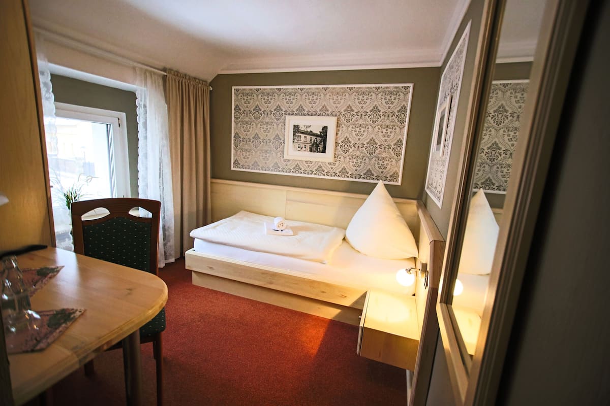 A hotel room with a bed, a bedside table, a chair, a lamp, and a wall with a framed picture.