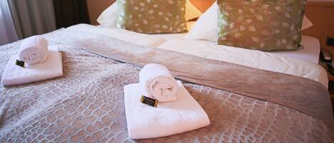 A hotel room with two beds, each with a rolled white towel and a pillow with a leaf pattern.