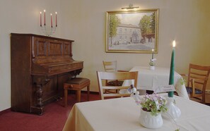 A room with a wooden piano, a table with a white tablecloth, chairs, a painting on the wall, and a candle. - Alter Krug Kallinchen (Zossen)