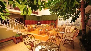 A spacious indoor area with multiple round tables and wicker chairs, a staircase, and a large tree providing shade. - Hotel Torres Touriño (Sanxenxo)