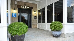 A hotel entrance with a sign reading "HOTEL" above the door, a wheelchair accessibility sign, and two large potted plants in front. - Hotel Torres Touriño (Sanxenxo)