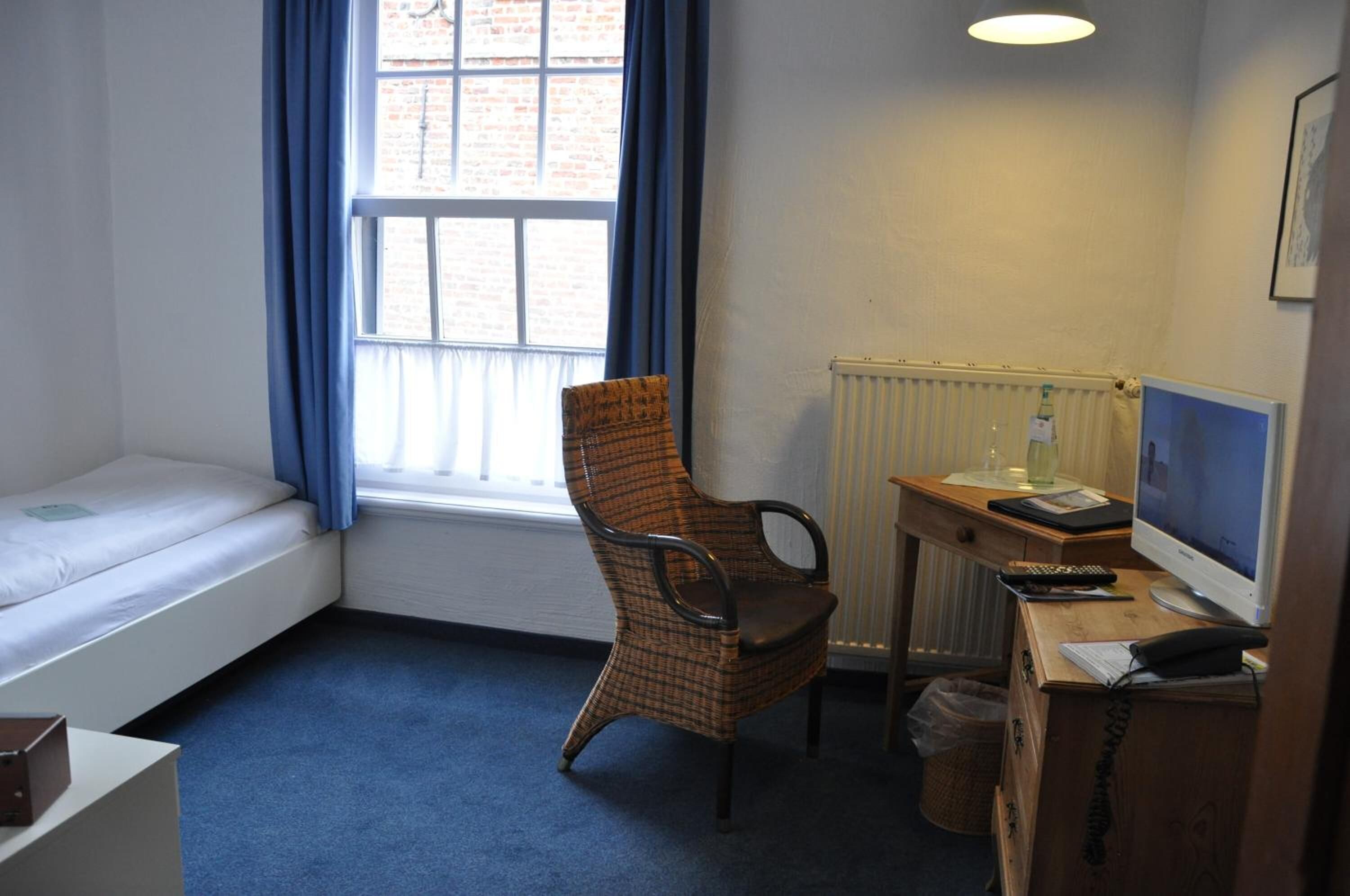 Una habitación pequeña con una cama individual, una silla, un escritorio con una computadora y una ventana con cortinas.