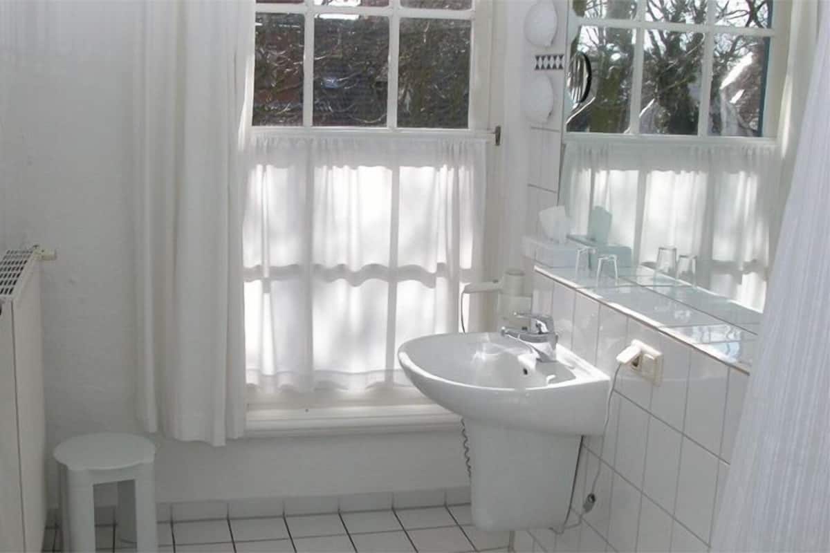 Une salle de bain avec un lavabo blanc, un miroir et une fenêtre avec des rideaux.