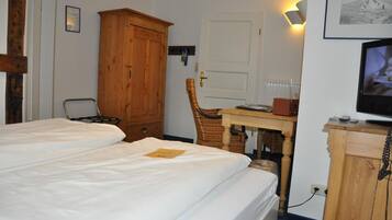 Quarto de hotel com duas camas, um guarda-roupa de madeira, uma secretária com cadeira, uma televisão e uma luminária na parede.