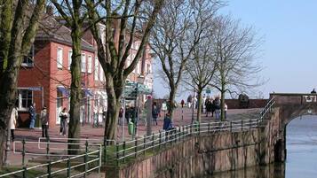 A riverside walkway with stone bridges, trees, and buildings.