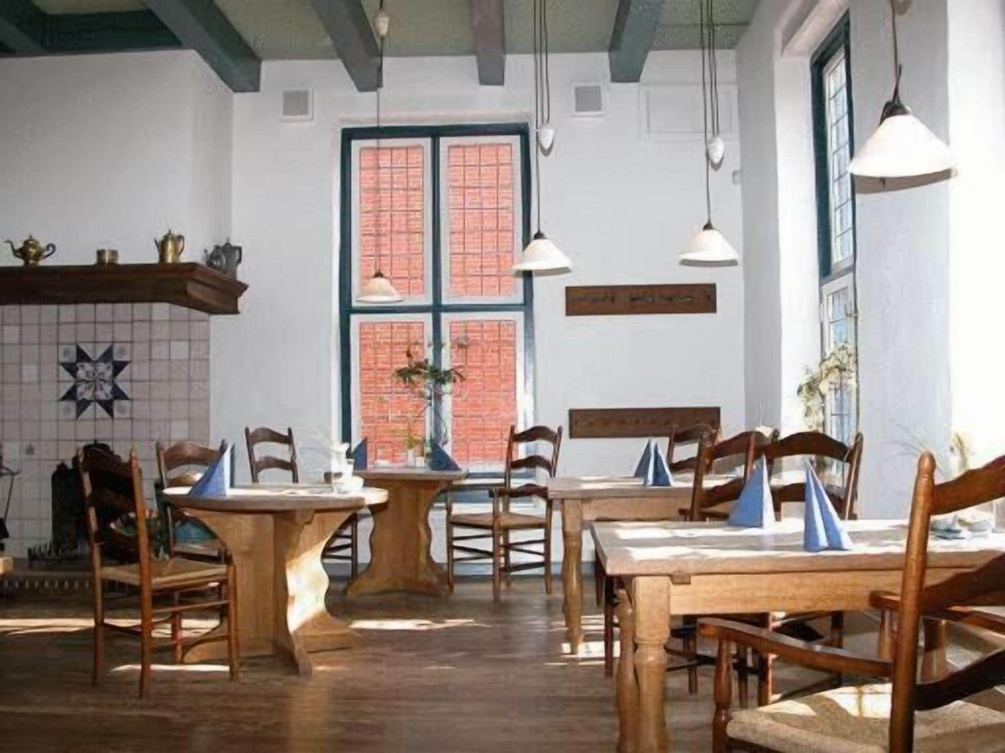 Un comedor con mesas y sillas de madera, pared de ladrillo y lámparas colgantes.