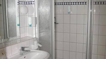 Un baño con un lavamanos blanco, un espejo y una ducha con mampara de vidrio.