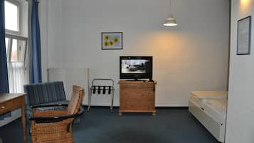 Una habitación pequeña y amoblada, con una televisión, un sofá, una silla, un aparador de madera y una cama.