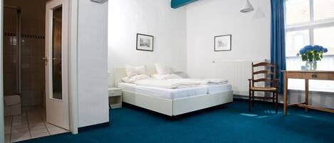 Quarto com cama, escrivaninha, cadeira e janela com cortinas.