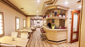 Een restaurantgedeelte in een hotel met houten tafels en stoelen, een bar met krukken, en een bordje dat een toilet aangeeft.