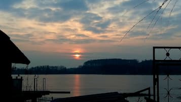 Tramonto su un lago tranquillo con un molo e una struttura con tetto di paglia sullo sfondo.