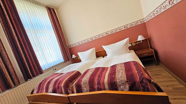 A hotel room with a bed, curtains, a nightstand, and a wall with a floral border. - Hotel Nordischer Hof (Krakow am See)