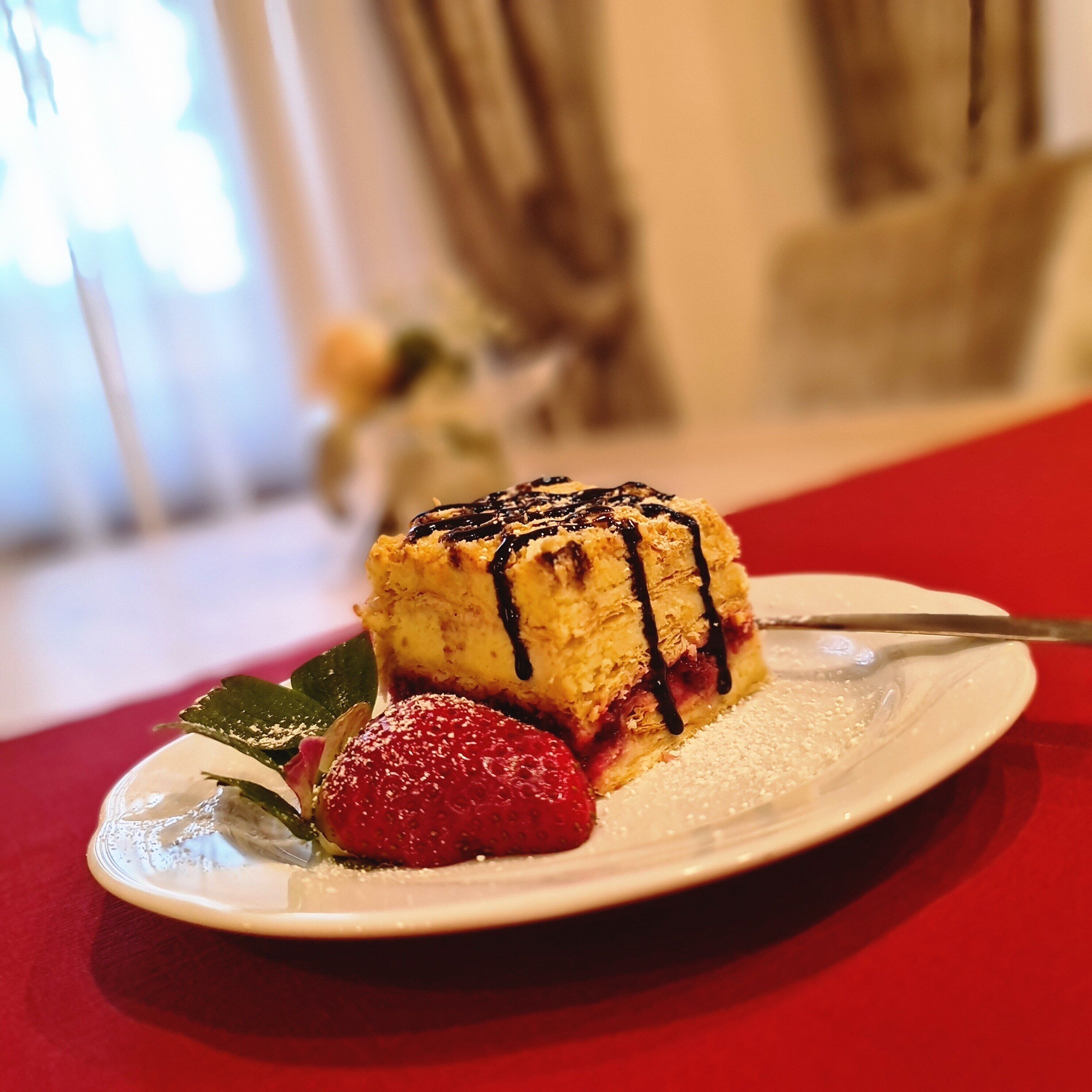 Une assiette à dessert avec une part de gâteau, une fraise et une pincée de sucre glace.