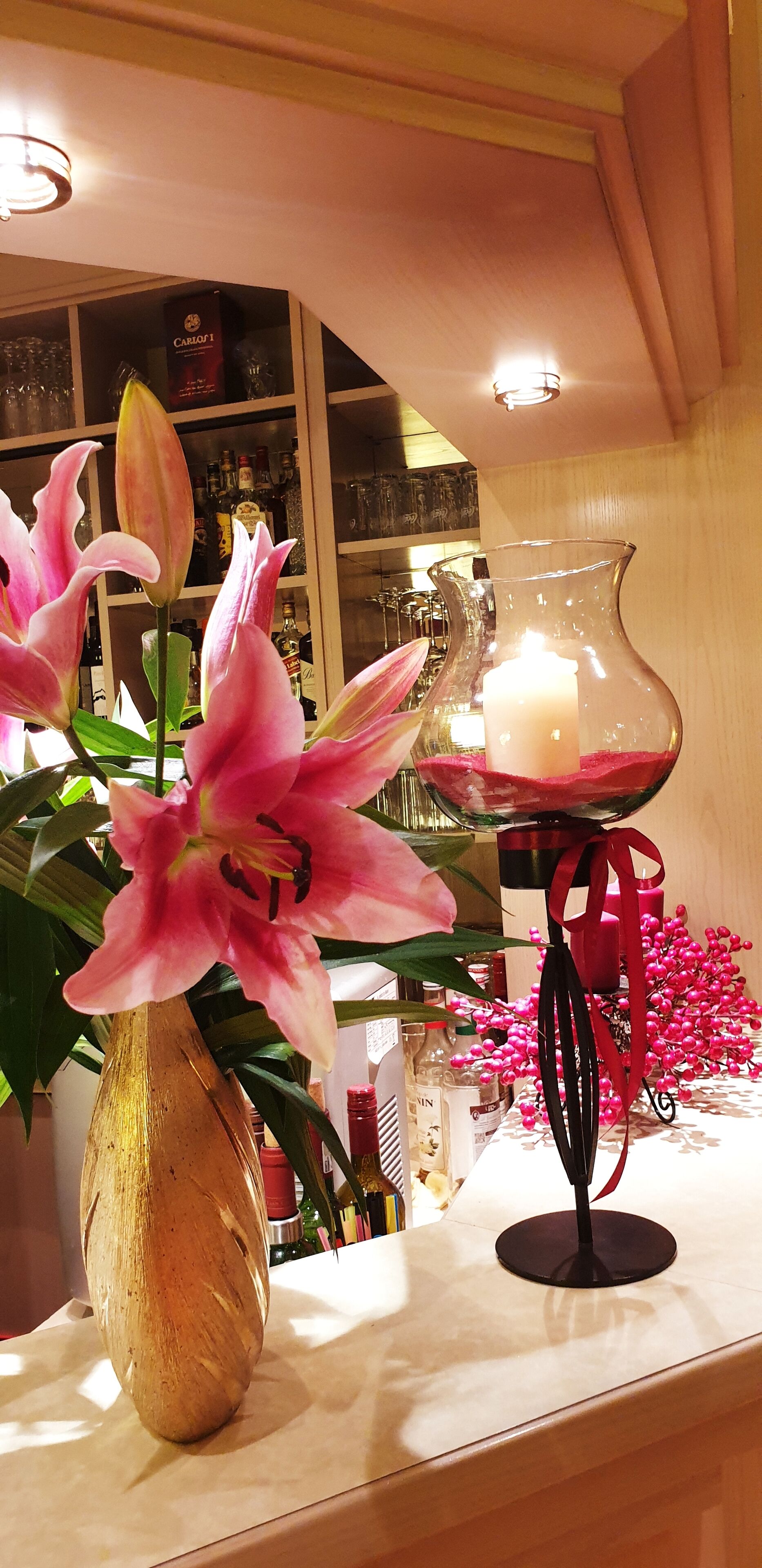 A table with a vase of pink lilies and a candle holder with a lit candle.