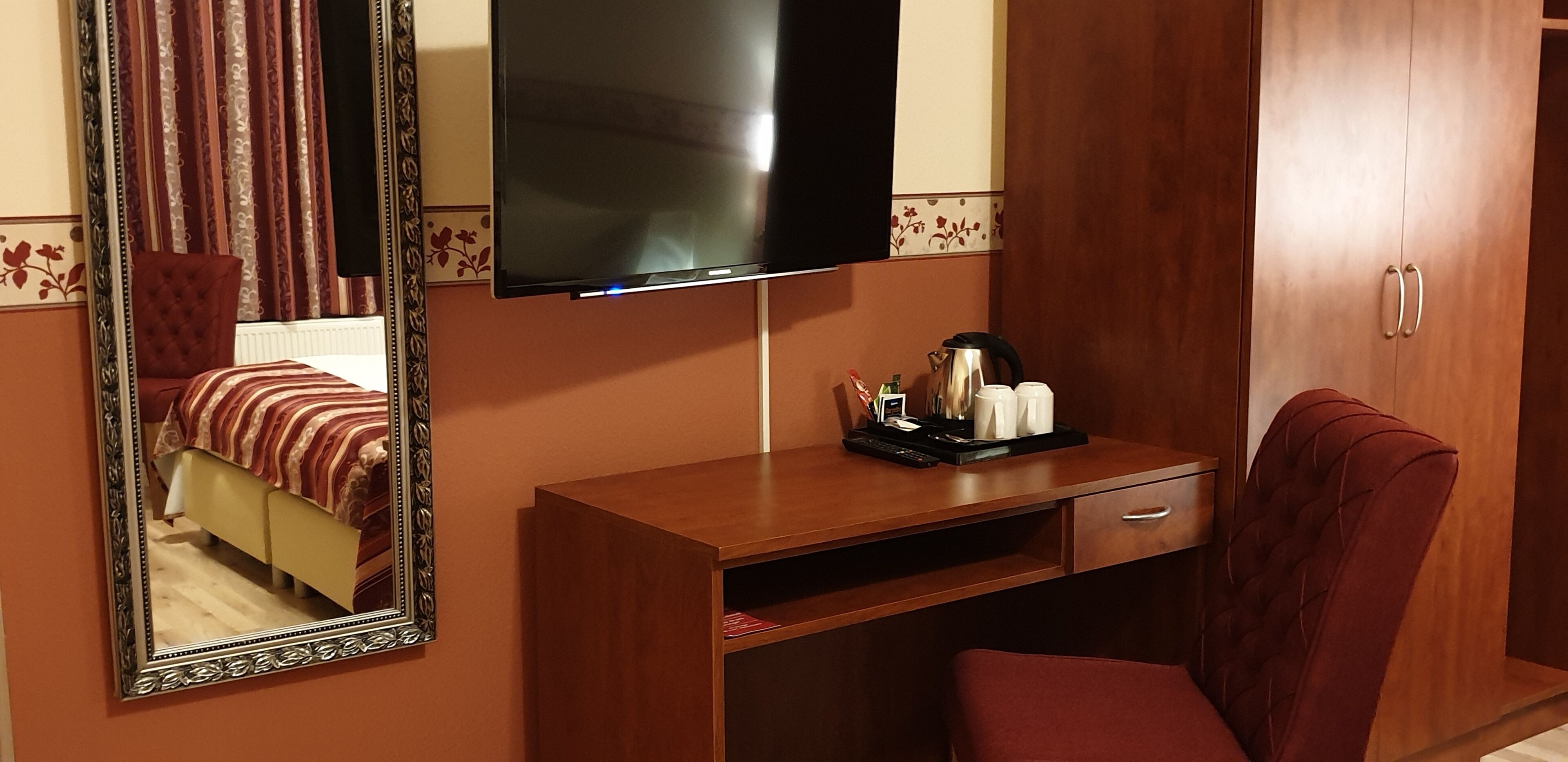 Habitación de hotel con cama, escritorio con televisor de pantalla plana, espejo, una silla roja y armario.