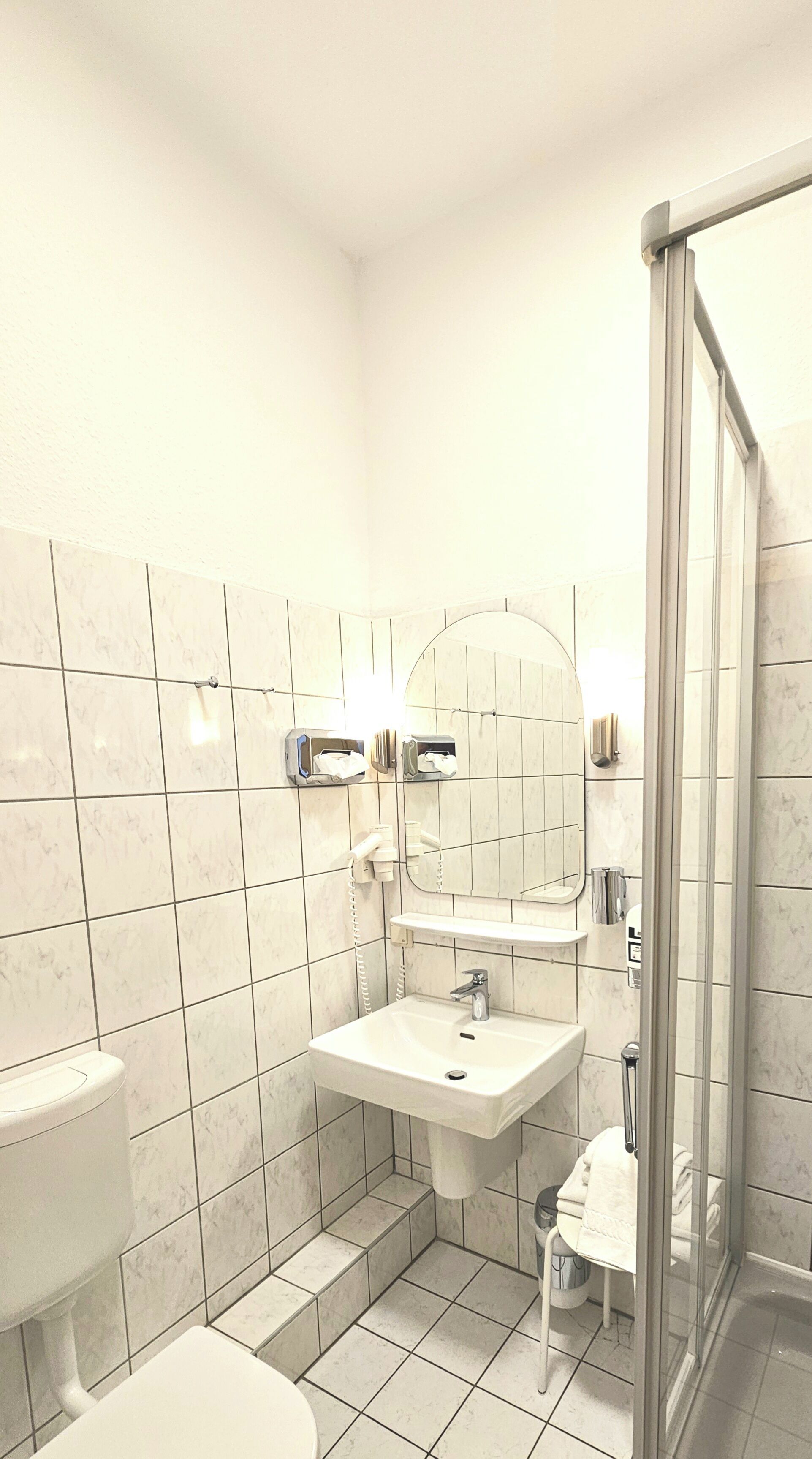 Un baño pequeño y limpio con inodoro, lavamanos y cabina de ducha de vidrio.