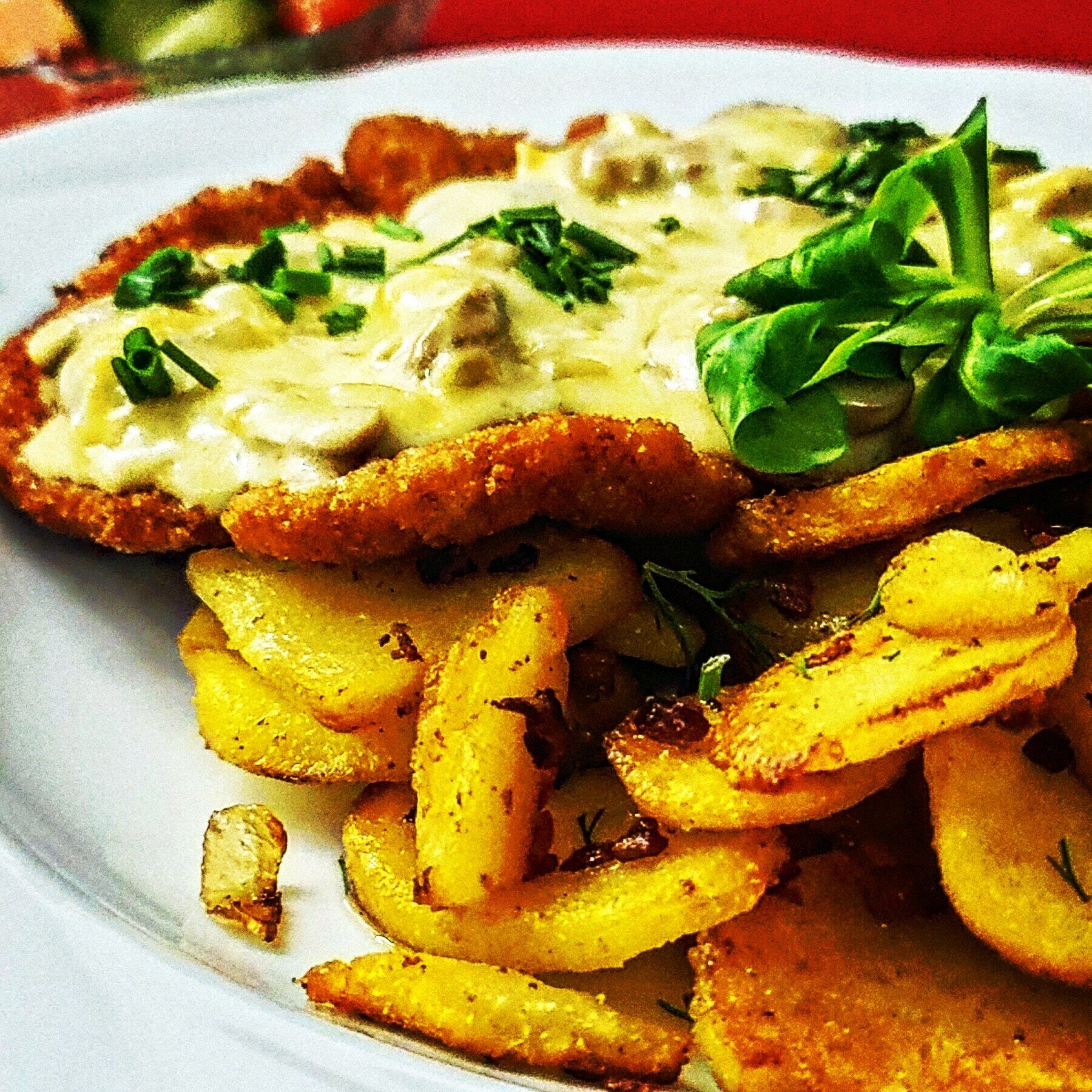 A plate with a breaded cutlet, mashed potatoes, and a green garnish.