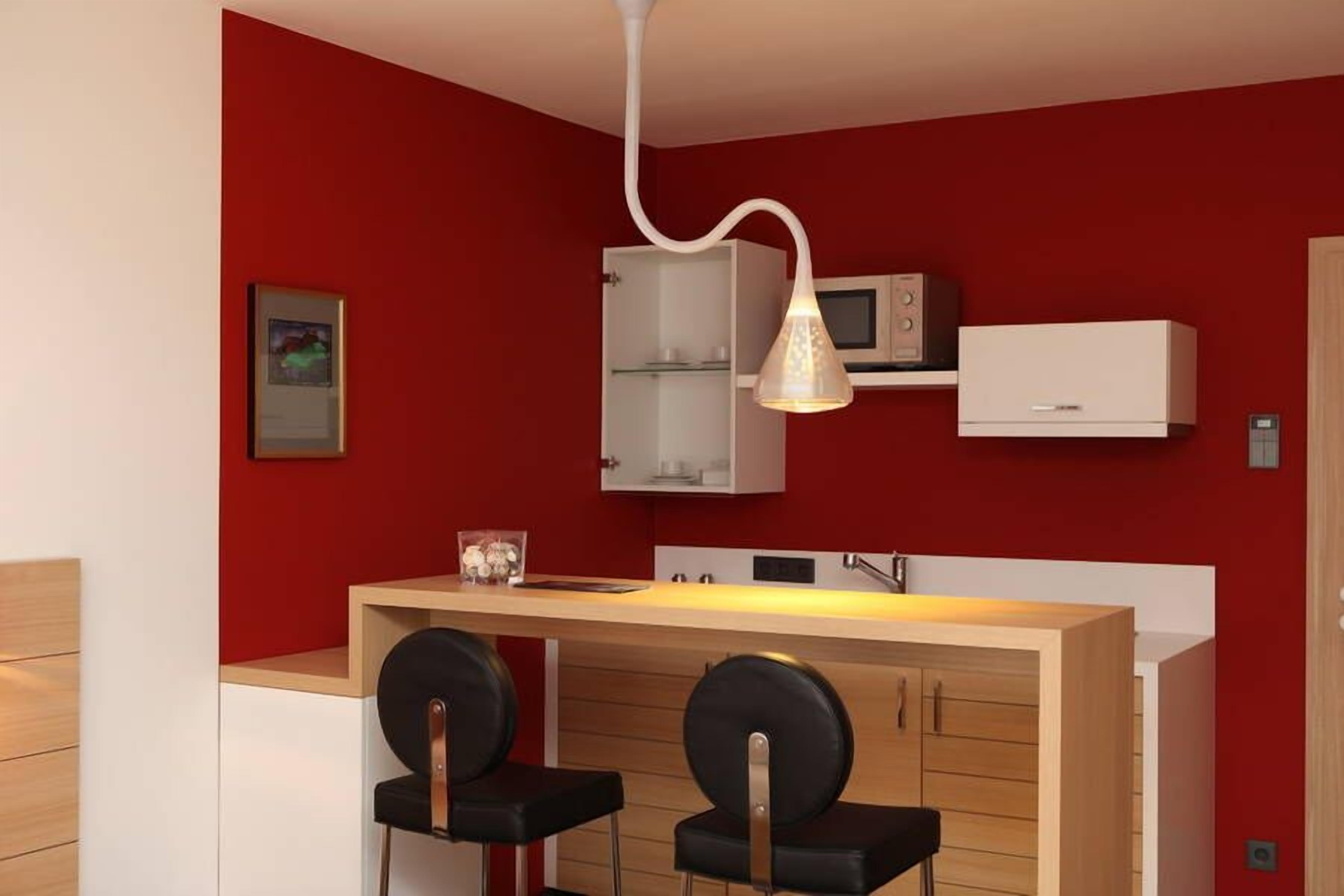 A compact kitchen with a red wall, white cabinets, a microwave, and a hanging light fixture.